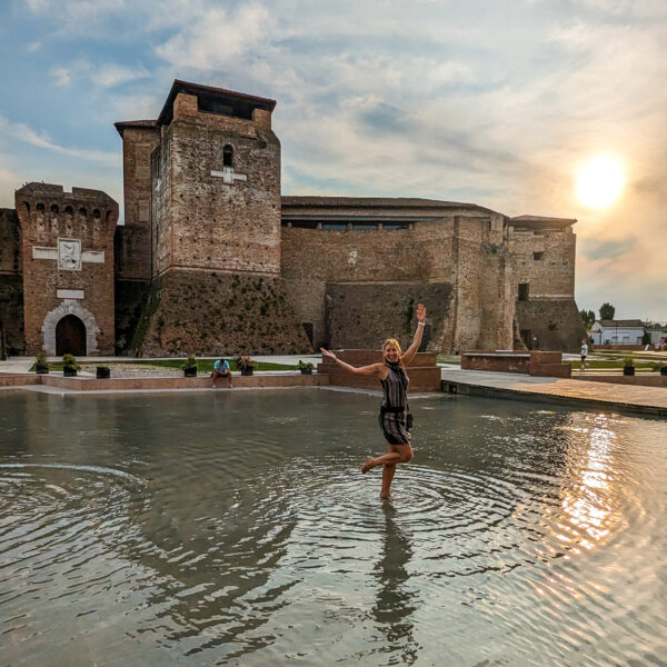 Meine Frau steht im flachen Wasser vor einer Burg in Rimini bei Sonnenuntergang