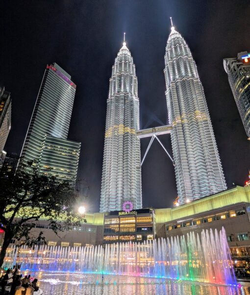 Die Petronas Towers bei Nacht, im Vordergrund bunt beleuchtete Wasserspiele