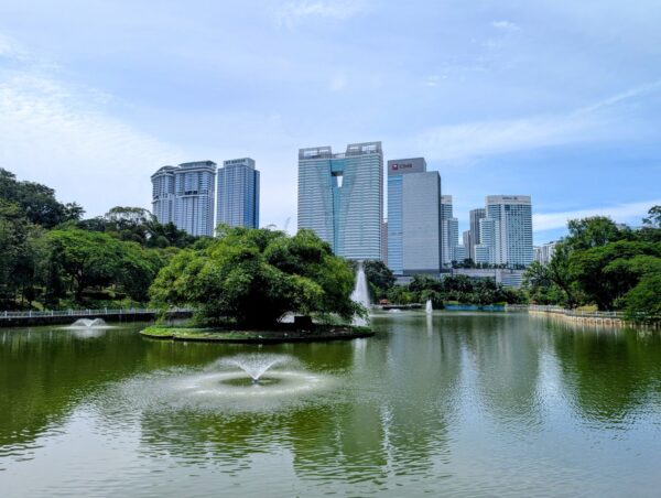 Im Botanischen Garten von Kuala Lumpur: Eine Wasserfläche mit Springbrunnen, im Hintergrund Hochhäuser. 